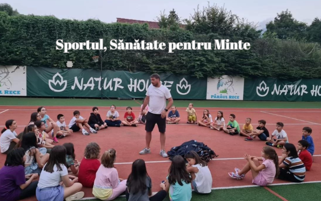 Un antrenor stă în picioare și vorbește unui grup de copii așezați în cerc pe un teren de tenis, subliniind valoarea sportului. Textul de deasupra se citește: "Sportul, Sănătate pentru Minte" (Sport, Health for the Mind).