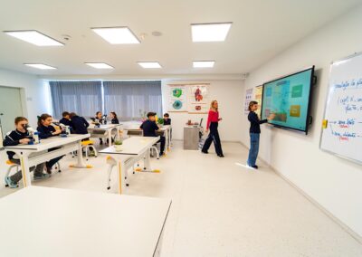 Un profesor observă cum un elev scrie pe o tablă digitală într-o sală de clasă din Scoala privata sector 3, în timp ce alți elevi lucrează la birouri cu microscoape.