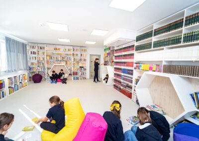 Copiii citesc și stau pe saci de fasole într-o bibliotecă luminoasă și modernă dintr-o scoală privată din sectorul 3, cu rafturi pe pereți.