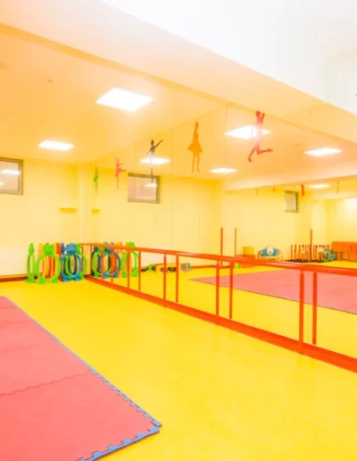 Studio de dans luminos cu pereți galbeni, oglinzi cu margini roșii, covorașe roșii și galbene și echipamente colorate stivuite în colț. Decalcomanii de balet împodobesc peretele cu oglinzi în această gradinita privata vibrantă din sectorul 3.